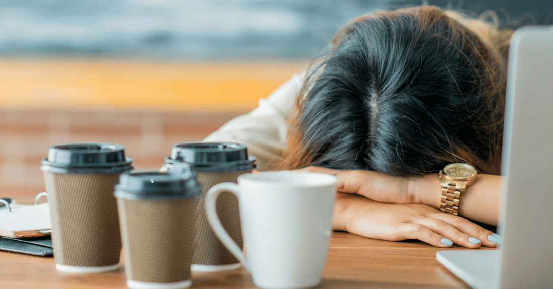 An exhausted woman rests her head on her desk.