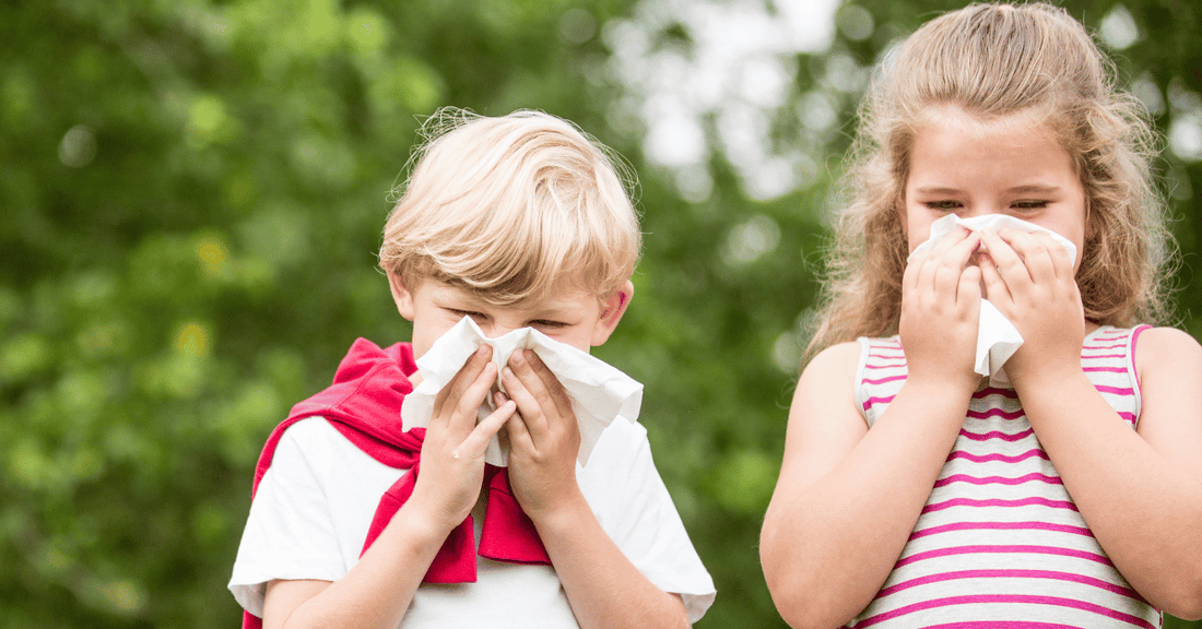 A boy and girl sneeze into tissues.