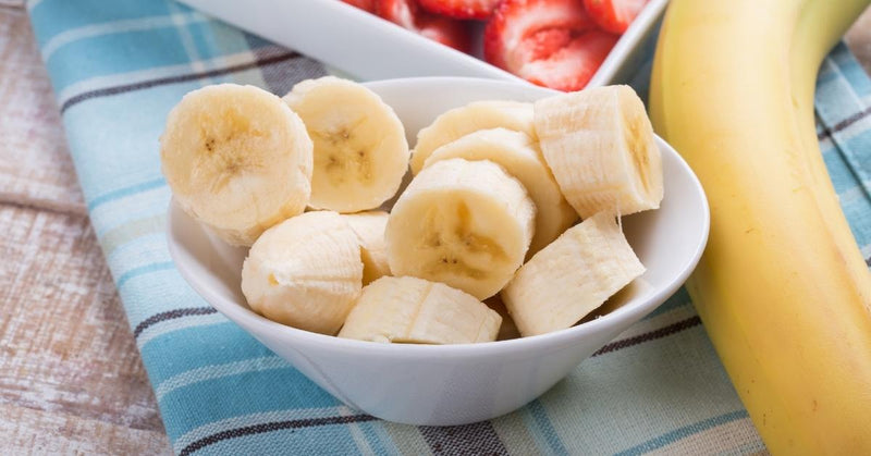 A bowl of banana slices next to a full banana.