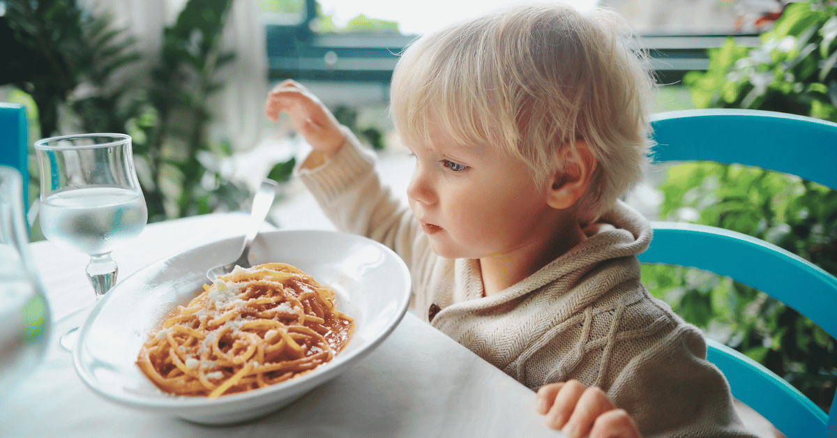 A young child eats a bowl of pasta.