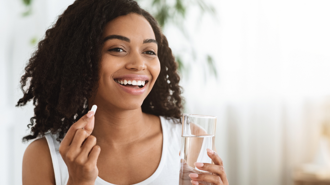 A smiling woman holds a health supplement and glass of water.
