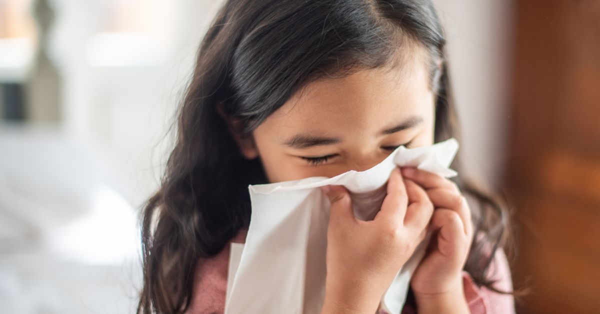 A girl holds a tissue to her nose.