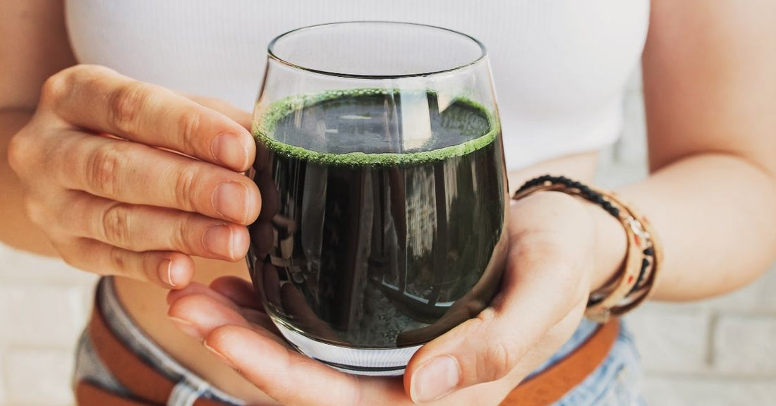 A woman holds a glass of water mixed with a microalgae  supplement.