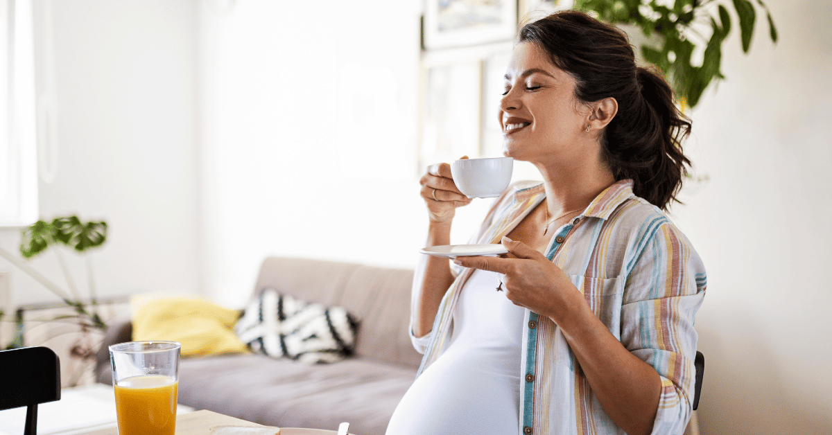 A pregnant woman drinks a cup of coffee.