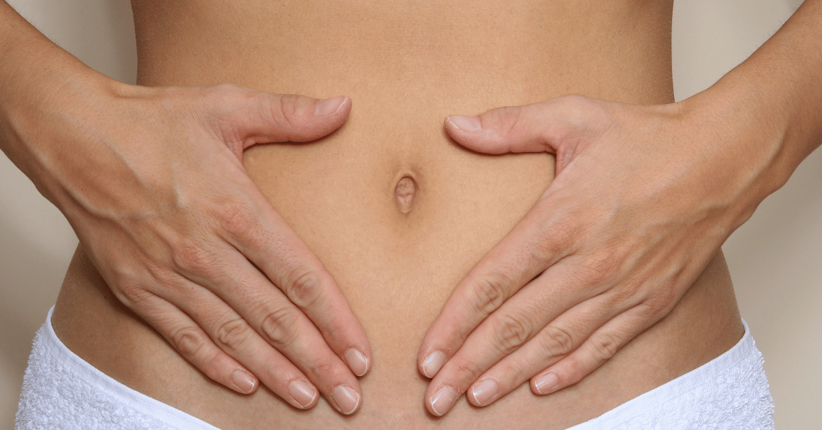 A woman rests her hands on her stomach.