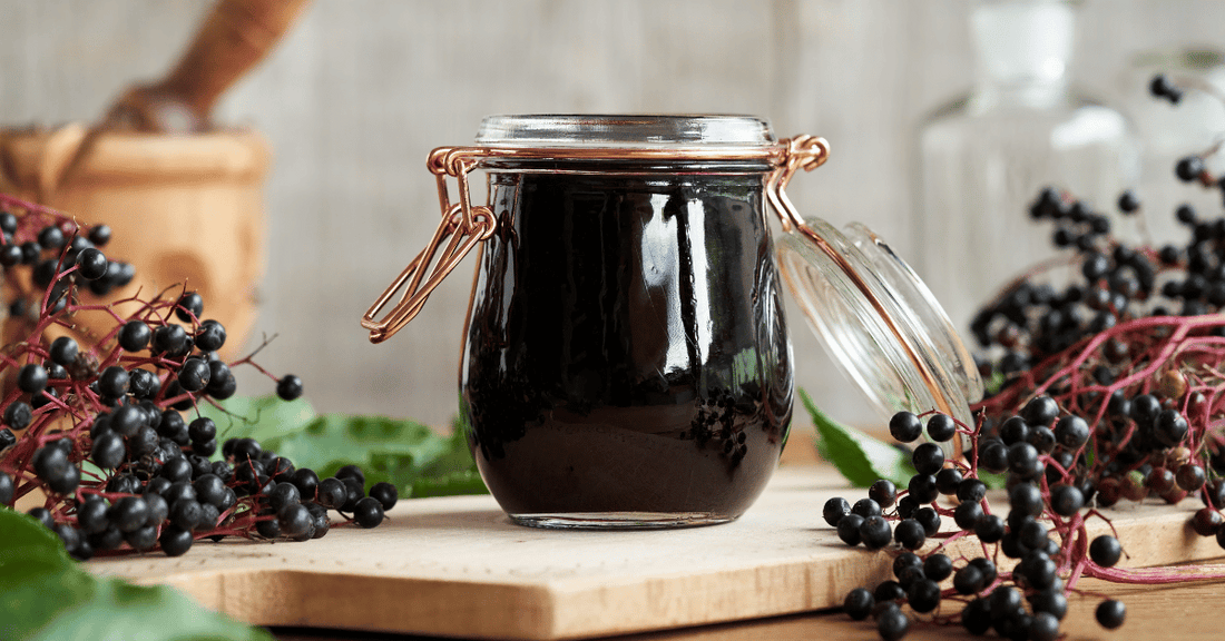 A jar of elderberry syrup surrounded by elderberries.