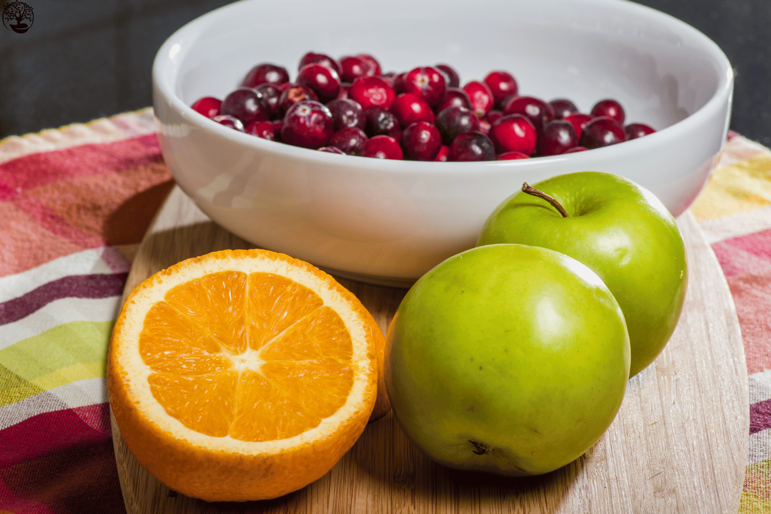 Cranberries, oranges, and apples on a colorful table cloth.