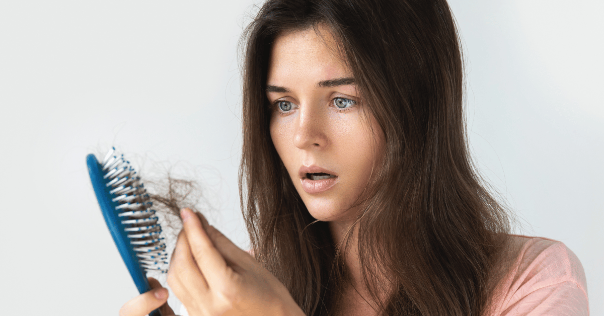 A woman in distress looks at the large amount of hair in her hairbrush. 