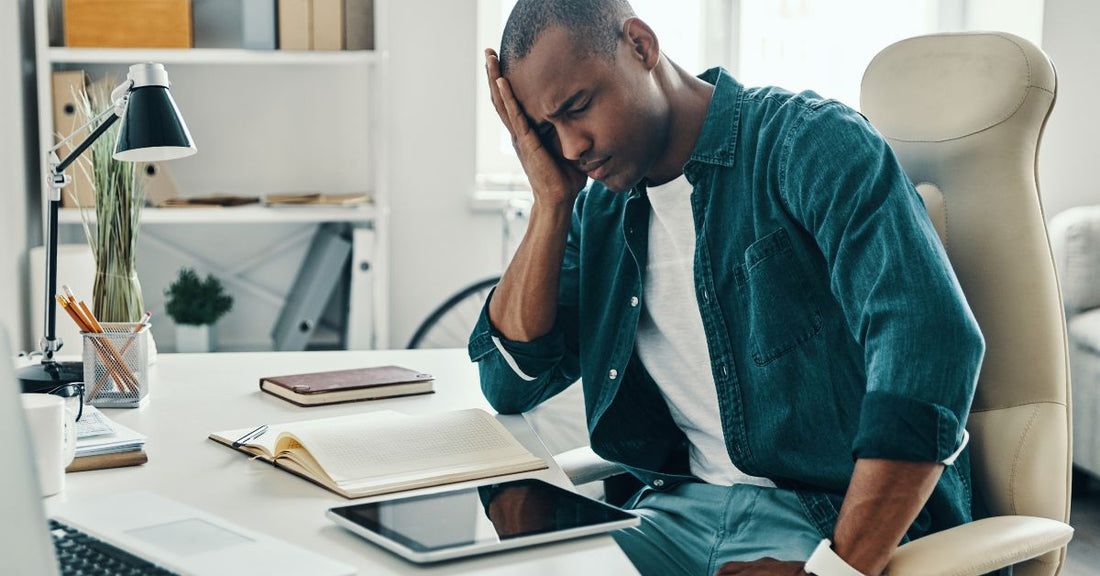 A man leans on his desk holding his head.