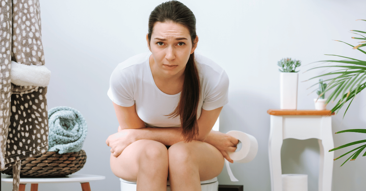 A woman in discomfort sits on a toilet.