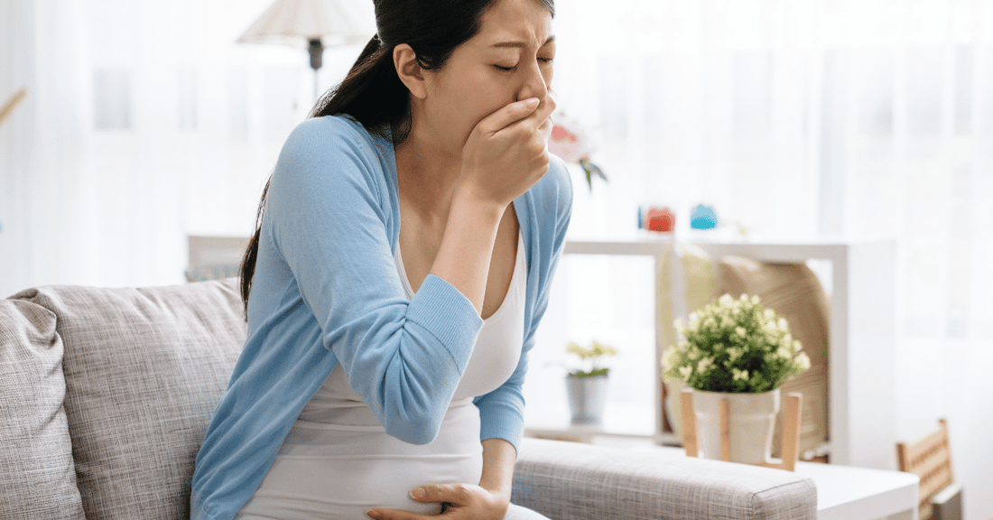 A pregnant woman experiences morning sickness while sitting on her couch. 