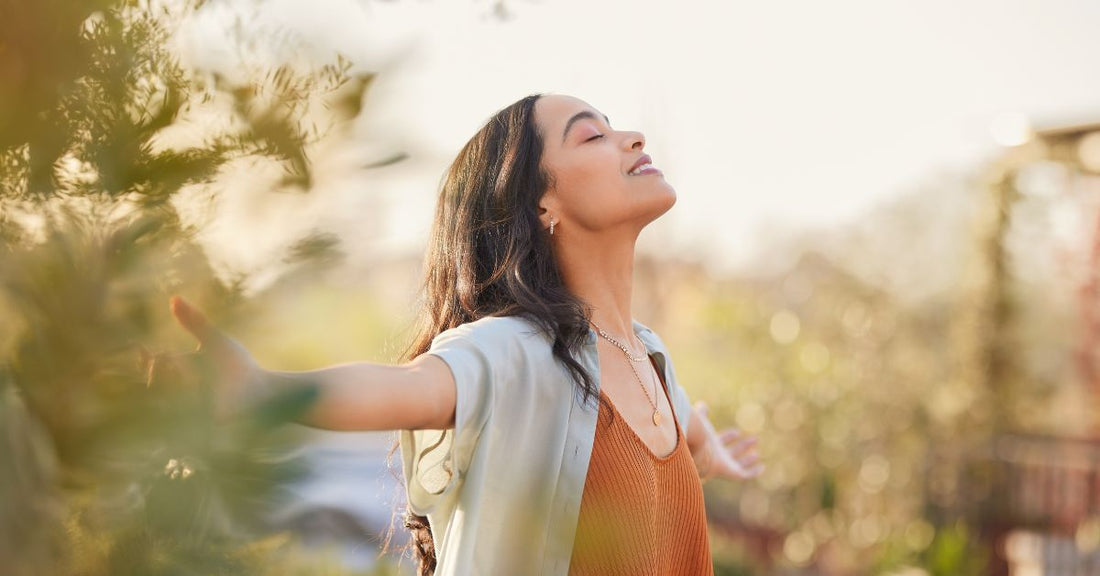 A woman peacefully stands outside in nature.