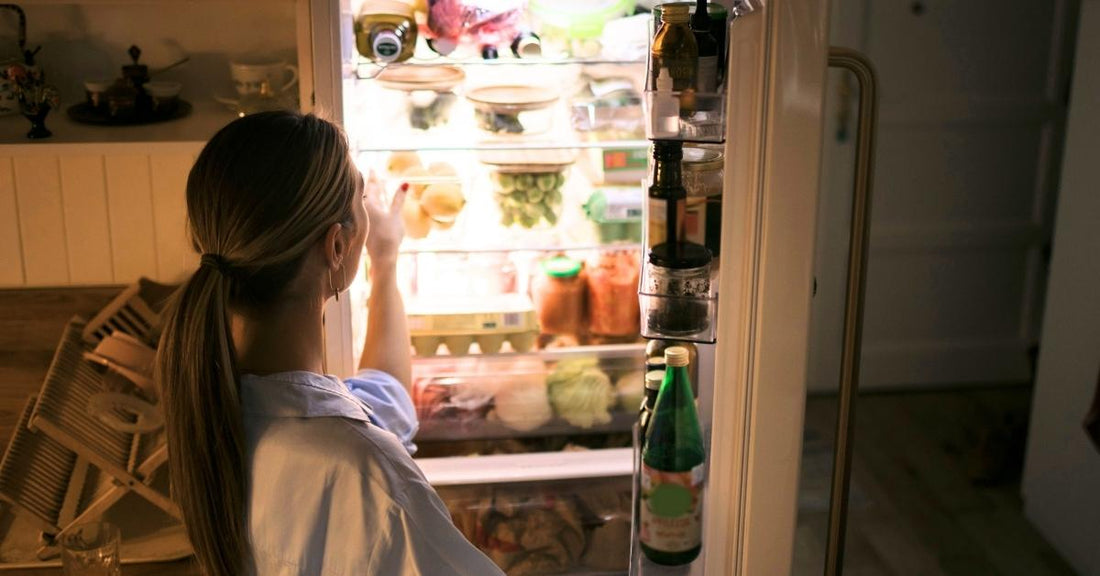 A woman gets food out of her fridge at night.