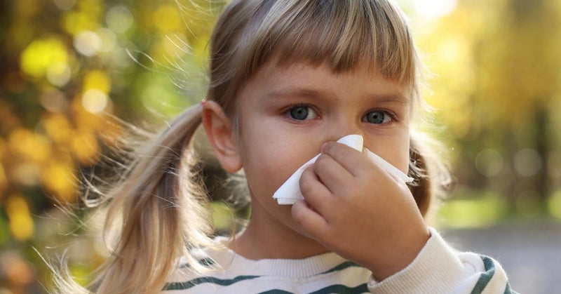A young girl holds a tissue to her nose.