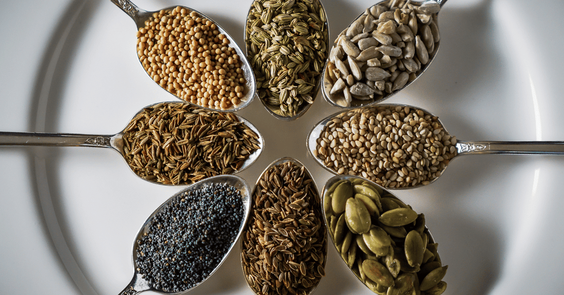 Spoonfuls of various seeds arranged in a circle on a white plate.