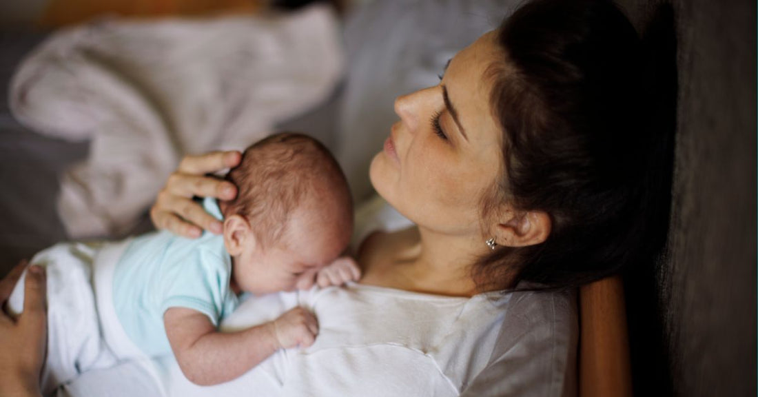 A tired mother rests while holding her infant.