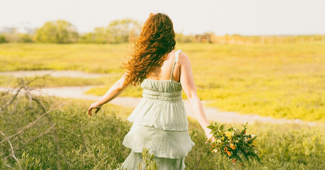 A woman walking through a field of tall grass in sunlight.