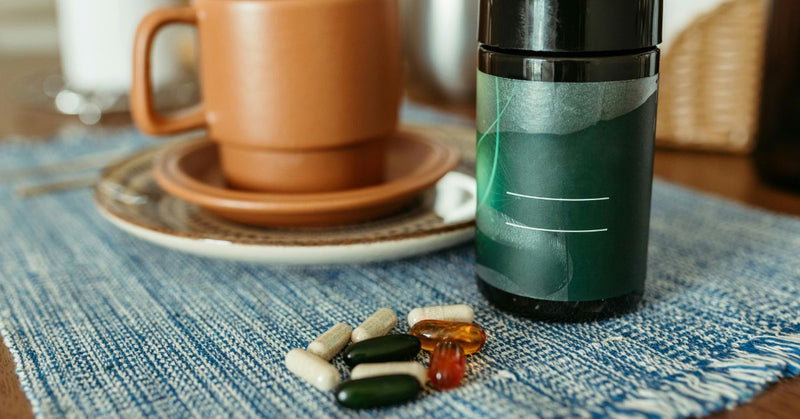 A handful of supplements lay on a placemat next to a cup of coffee.