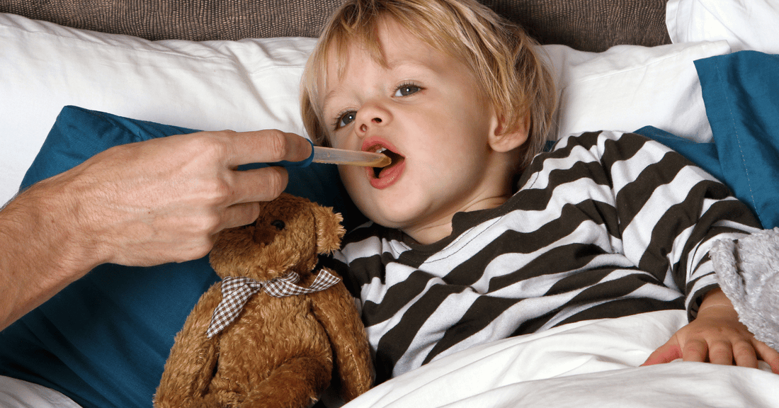 A boy takes some medicine while laying in bed.