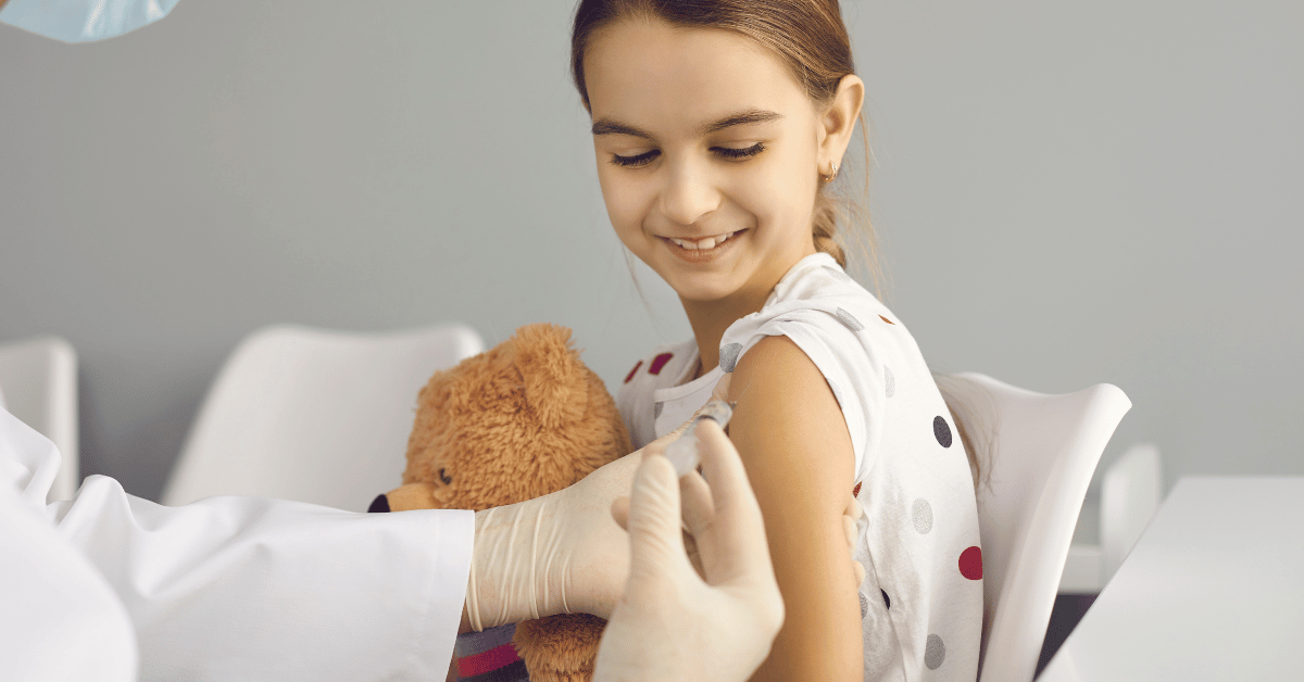 A smiling girl gets a shot in her arm.