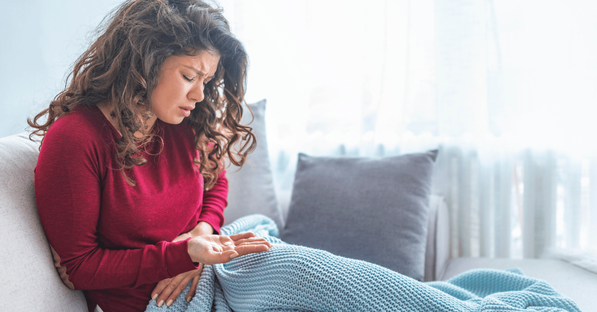 A woman holds pain medicine in her hand while holding her abdomen.