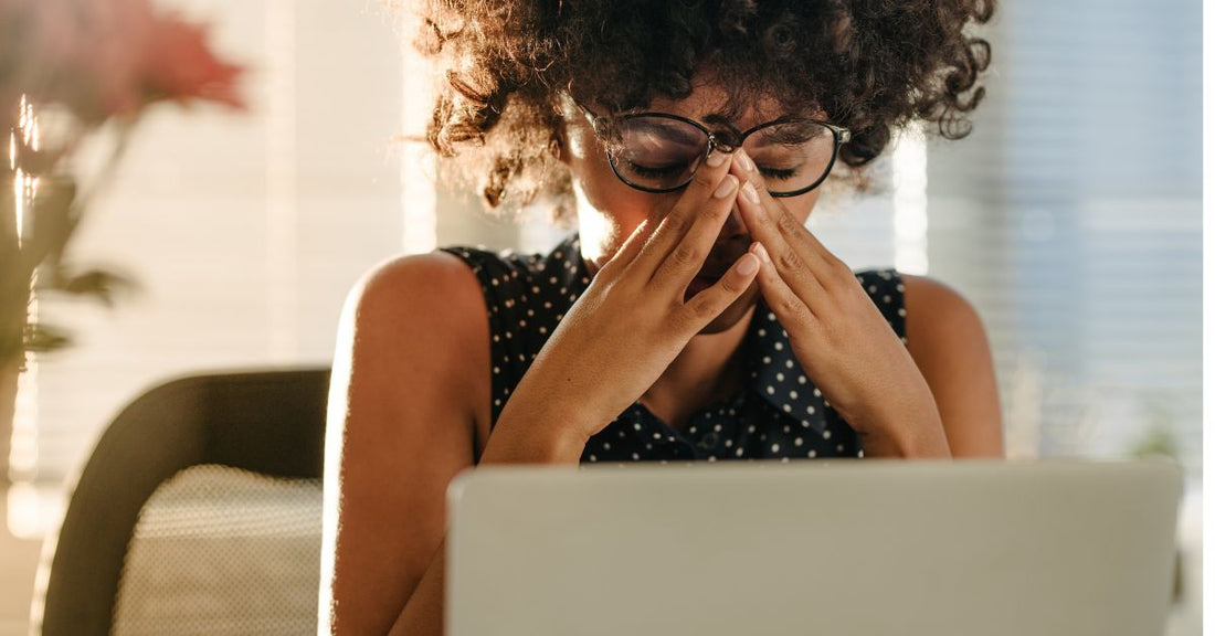A stressed woman rubs her forehead while she sits in front of her computer.